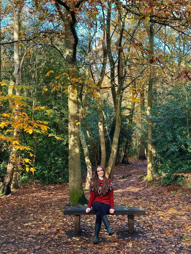 A woman sitting on a bench in the woods surrounded by trees.