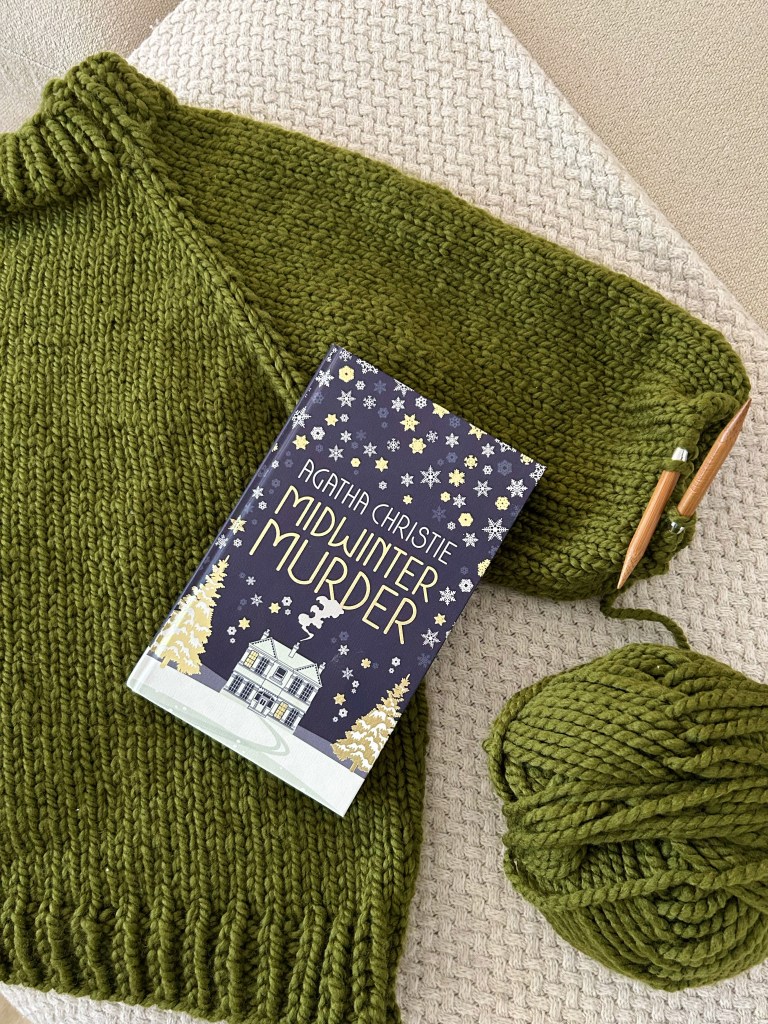 A winter-themed book on top of a half-knitted handmade green jumper, on a beige blanket and sofa.